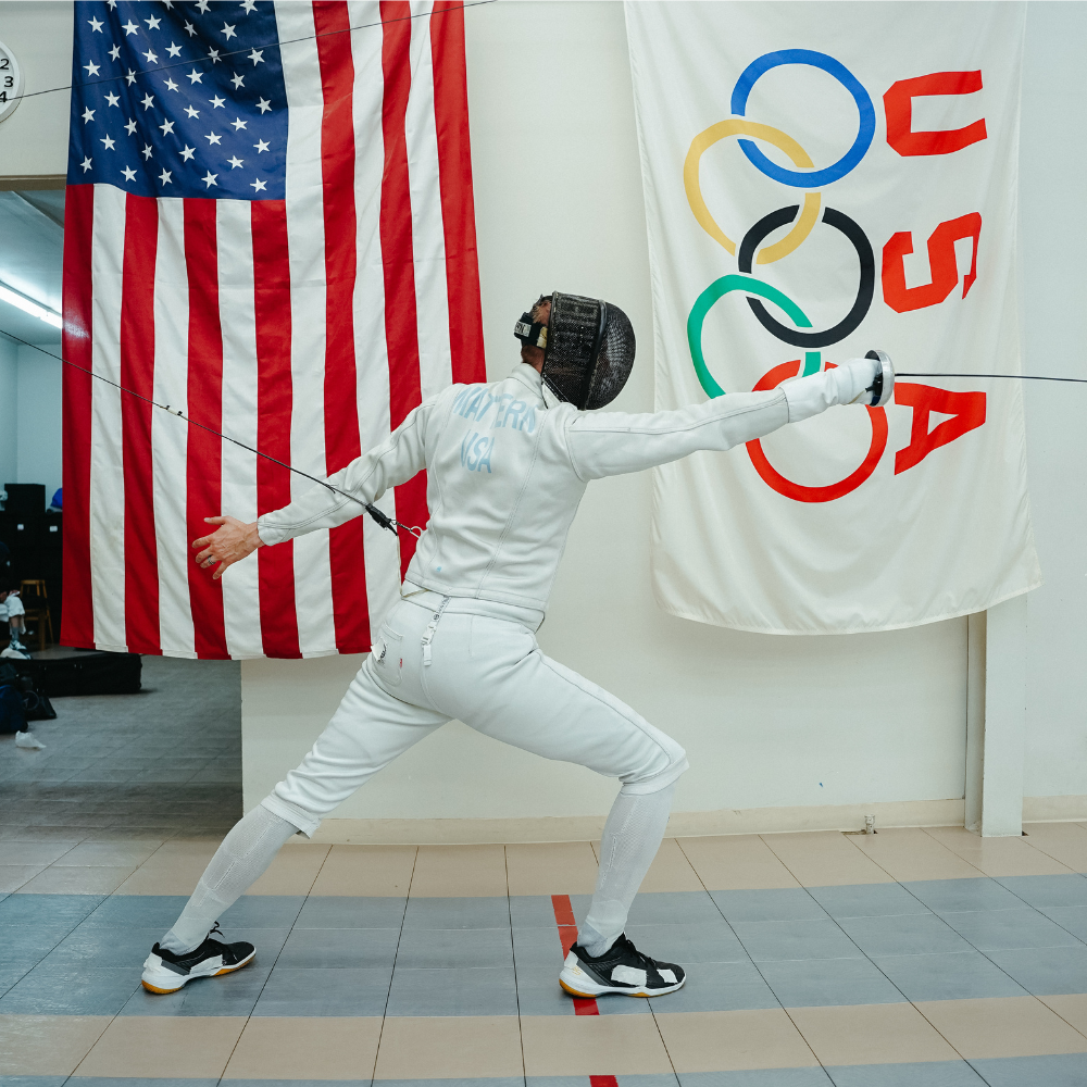 Cody Mattern in a fencing stance in front of USA and IOC flags