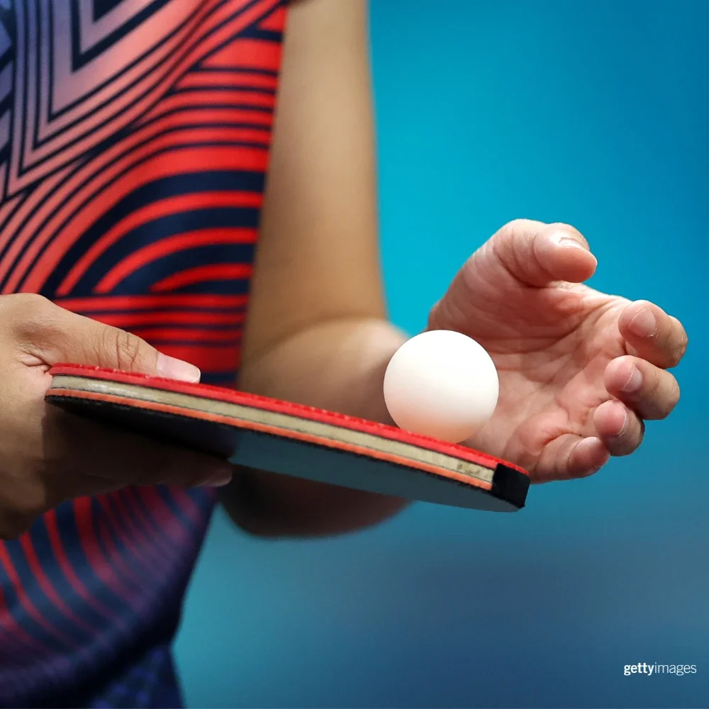 Photo of a person's hand holding a ping pong paddleboard and ping pong ball